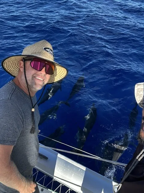 Guest grinning at the rail with a pod of dolphins alongside