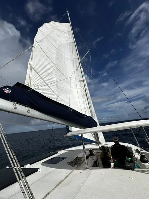 Mainsail raised on a catamaran, crew working the cockpit